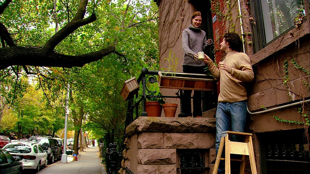 中镜头倾斜的男人在梯子上工作窗户/女人给男人端咖啡/女人挥手/布鲁克林，纽约视频下载