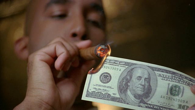低角度的特写男子点燃雪茄与100美元的纸币/呼出的烟雾视频下载