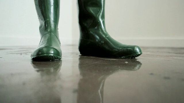 穿着雨靴的女人走在被水淹没的地板上视频下载