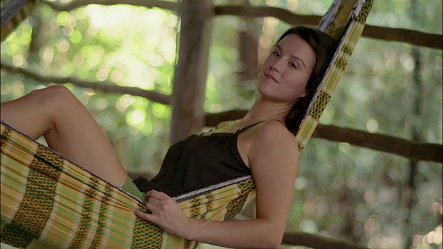 中镜头女子躺在吊床上放松/对着镜头微笑/巴西亚马逊河视频素材
