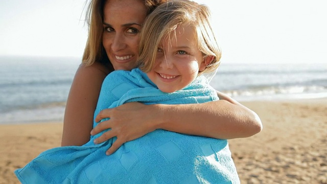母亲抱着女儿在海滩上的蓝色毛巾视频素材