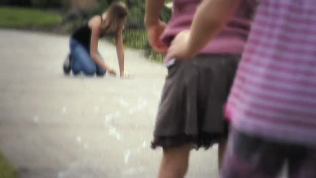 一个女孩用粉笔在人行道上画跳房子，两个女孩跳着玩跳房子/加拿大不列颠哥伦比亚省兰利。视频素材