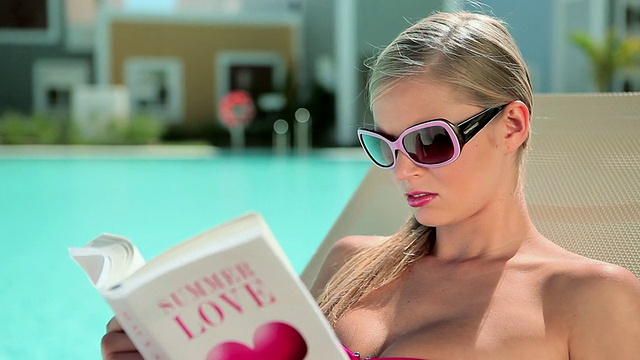 一个女人在泳池边的日光躺椅上看书视频下载