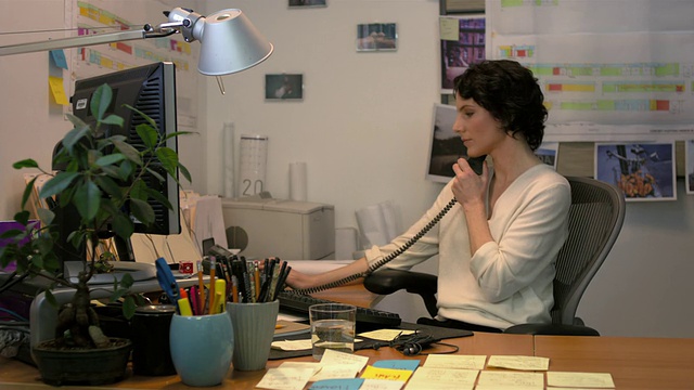 中镜头锁定女商人坐在办公桌前，敲击电脑键盘，讲电话视频素材