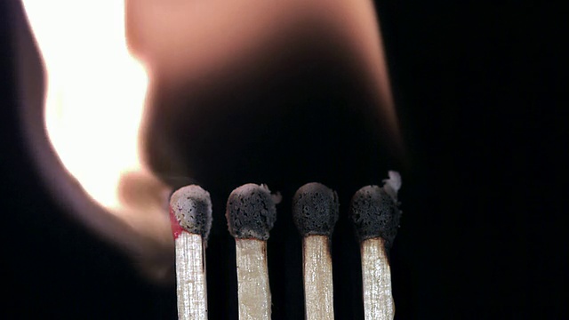 四根点燃和燃烧的火柴，在黑色背景下连续点火，慢动作视频素材