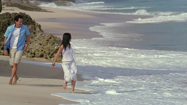 慢动作宽镜头夫妇在海滩上跑步/印尼巴厘岛视频素材