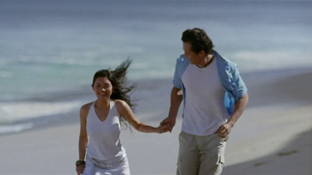 慢镜头宽镜头夫妇在海滩上跑步，潮水来了/巴厘岛，印度尼西亚视频素材