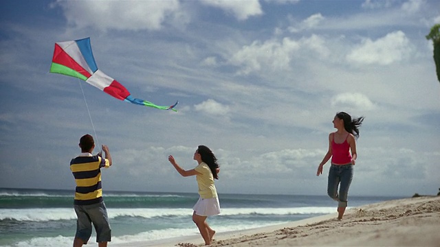 一名男子和两名女子在印尼巴厘岛的海滩上放风筝视频素材