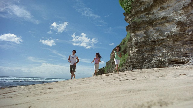 慢镜头广角拍摄两名妇女和男子跑向相机在海滩/巴厘岛，印度尼西亚视频素材