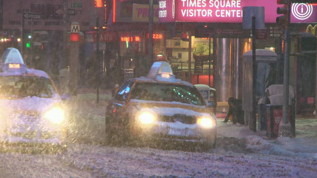 在暴风雪的夜晚，汽车缓慢地驶过时代广场。视频素材