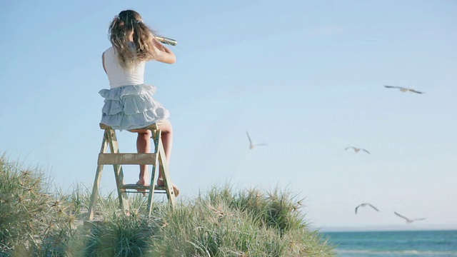 在澳大利亚维多利亚州的墨尔本，一个女孩坐在梯子上，通过望远镜看海滩视频下载