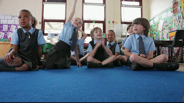 洛杉矶小学生坐在教室地板上急切地举起手/英国，大雅茅斯视频下载
