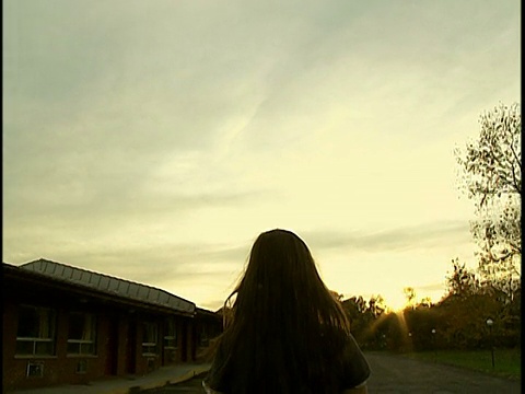 中镜头年轻女子，棕色长发在夕阳下飘过空旷的停车场视频素材