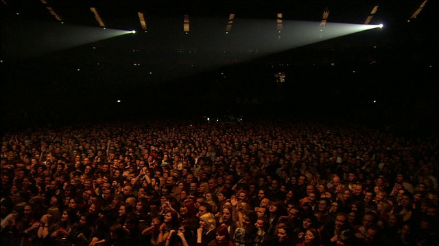 在英国伦敦的O2舞台上，人群沐浴在橙色的灯光下，面向舞台享受表演视频素材
