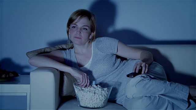 MS, ZI, CU，一个年轻的女人斜靠在沙发上，一边看电视一边吃爆米花视频下载