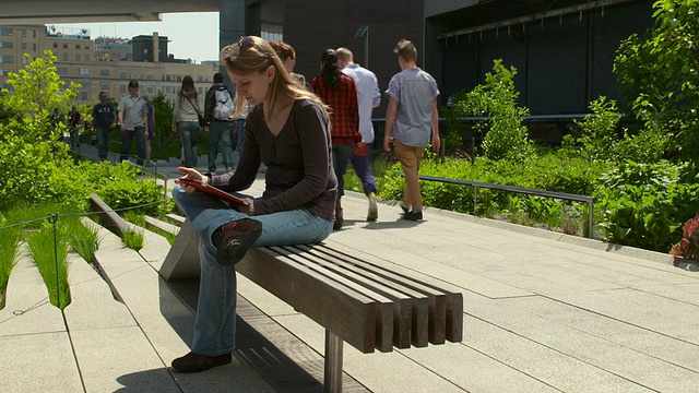 一名女子坐在高架公园的长椅上，在IPad上看书。视频素材