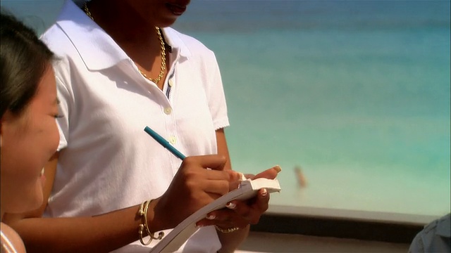 在巴哈马群岛的港湾岛度假期间，一对年轻的情侣在海边餐厅从服务员那里点餐视频下载