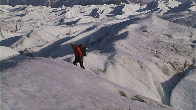极端长镜头泛左倾斜放大-一个冰上攀岩者走上一个冰冻的斜坡/阿拉斯加，美国视频素材