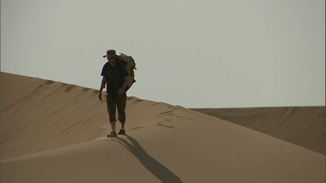 中等长镜头静态-一个徒步旅行者背着背包走过撒哈拉沙漠/撒哈拉沙漠，埃及视频素材