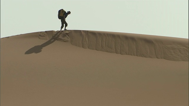 一名徒步旅行者背着背包走到埃及撒哈拉沙漠的沙丘顶部视频素材