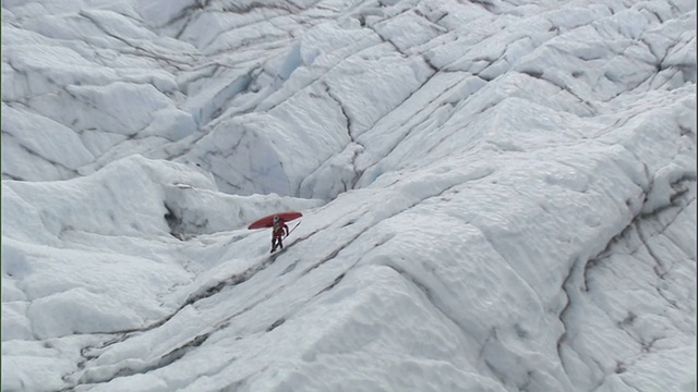 高空拍摄——美国阿拉斯加，一名男子背着皮划艇穿过一片巨大的冰面视频素材