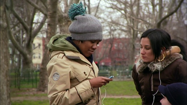 美国纽约布鲁克林区公园/威廉斯堡，年轻女性分享耳机，用MP3听音乐视频素材