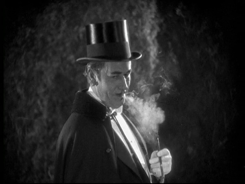 1925年CU B/W男子披着斗篷，戴着大礼帽，晚上在花园里抽烟视频素材