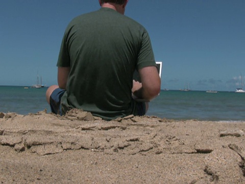 一名男子在海滩度假时使用笔记本电脑，走向水中视频素材