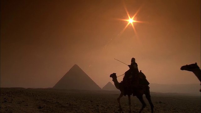 日落时骑骆驼的两个人的剪影，背景是吉萨金字塔，后视图，吉萨高原/吉萨，埃及视频下载
