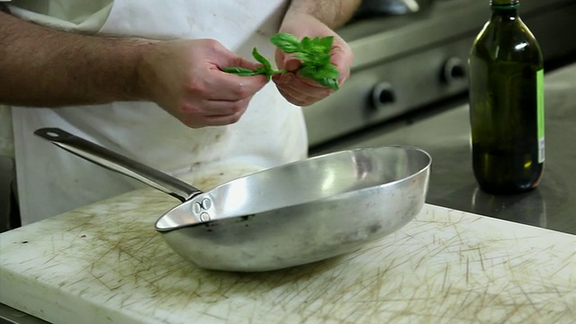 厨师将新鲜的罗勒放入油煎锅的特写镜头视频素材