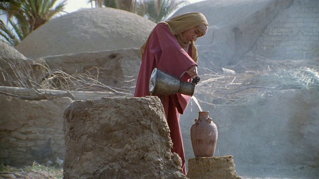 中东，一名男子站在井旁，往花瓶里倒水视频下载