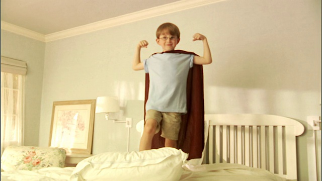 MS，男孩(6-7)穿着超级英雄披风在床上弯曲肌肉，肖像视频下载