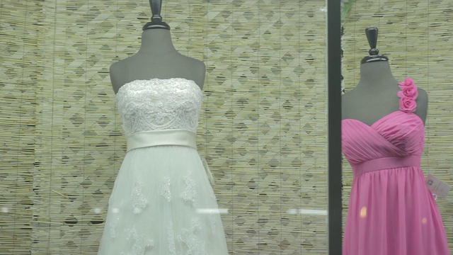 一件婚纱和三件伴娘礼服在晚上的橱窗里。视频下载