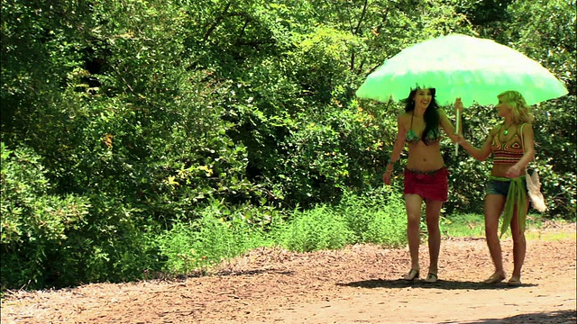 两个女孩在德克萨斯州的遮阳伞下走在土路上视频下载
