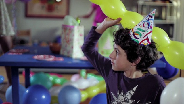 美国加州圣塔莫尼卡，一个带着派对帽的微笑男孩，拿着气球，看着摄像机，然后走了视频素材