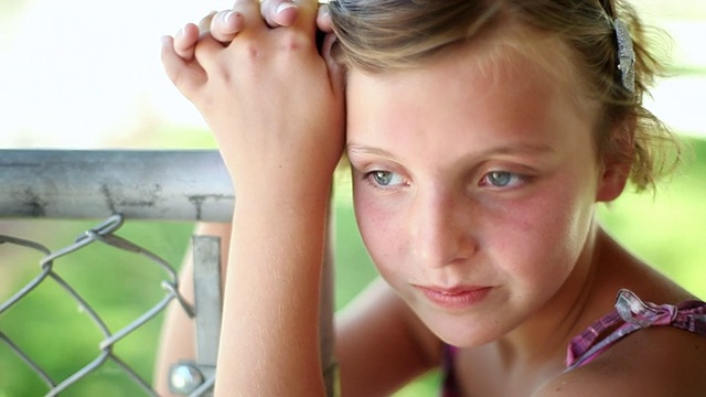悲伤的小女孩倚靠在篱笆柱上，看向别处/特雷西，加州，美国视频素材
