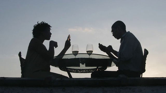 日落时分，一对夫妇在屋顶露台上使用手机的低角度视图视频下载
