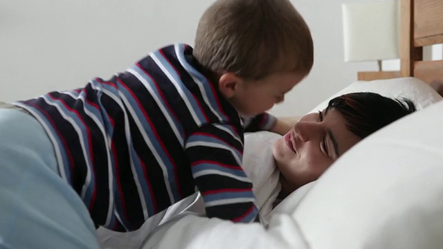 妈妈睡着了，男孩爬到床上，用亲吻和拥抱把妈妈叫醒视频素材