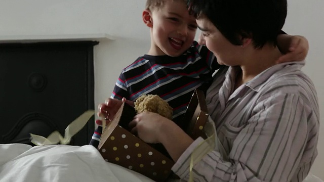 小男孩给躺在床上的妈妈一个礼物，并帮助她打开它视频素材