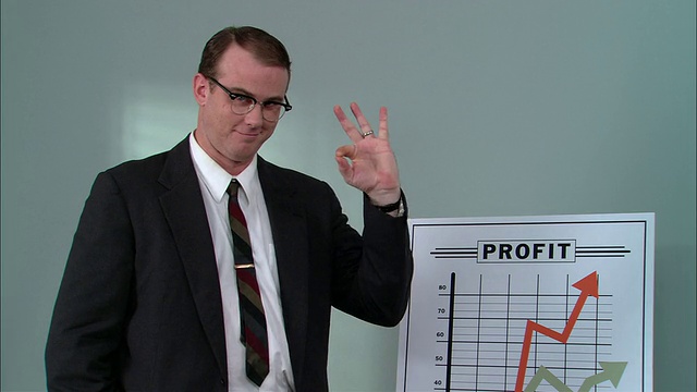 MS肖像商人站在显示利润增长的图表旁，竖起大拇指和OK手势，扣上夹克的扣子，系直领带/纽约市视频素材
