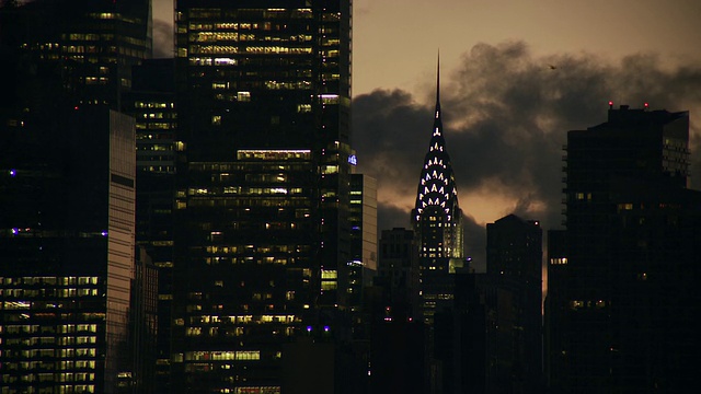 静态镜头的克莱斯勒大楼和邻近的天空照亮摩天楼，太阳升起在阴云密布的曼哈顿天空视频素材