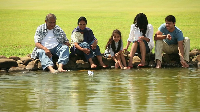 一家人坐在湖边，漂着一只纸船视频素材