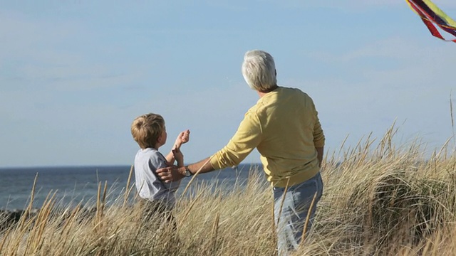 图女士爷爷教孙子放风筝在海滩沙丘/伊斯特维尔，弗吉尼亚州，美国视频素材
