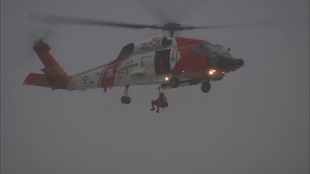 长镜头倾斜-一架海岸警卫队直升机盘旋，一名机组人员被吊降视频素材