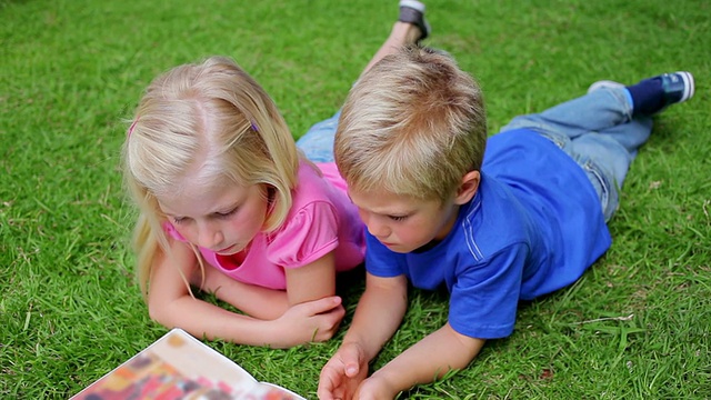 弟弟和妹妹躺在草地上看书视频素材