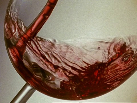 红酒倒入一个倾斜的玻璃杯底部，白色的背景，旋转的液体，有些溢出视频素材