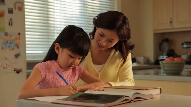 母亲在厨房/中国帮助女儿做作业视频素材