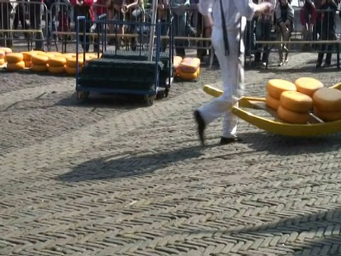 荷兰阿尔克马尔历史悠久的奶酪市场上，人们拿着大轮奶酪视频下载