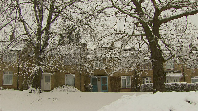 MS pan正穿过被雪覆盖的房屋，前景中厚厚的积雪中的树木，英国视频下载
