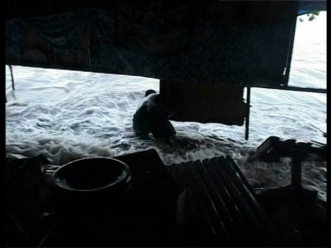 海浪滚滚而来时，一名男子紧紧抓住房子的支柱，基里巴斯，中太平洋。视频下载
